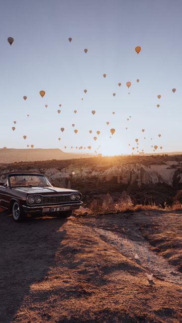 Vintage convertible with hot air balloons in Göreme, Turkey at sunrise.