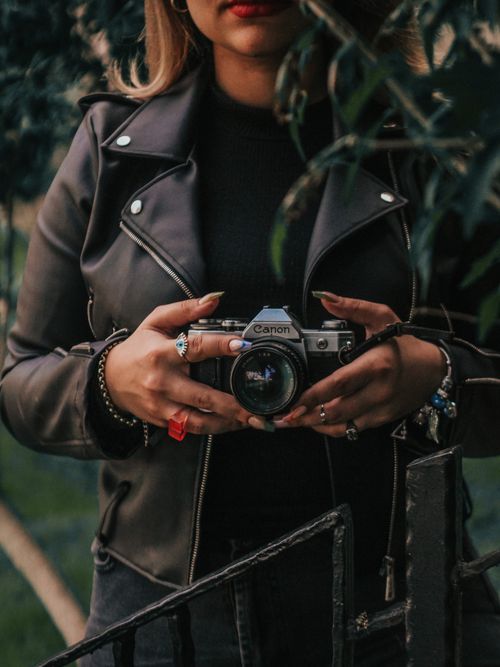 Free Stylish woman in a leather jacket holding a vintage camera outdoors. Stock Photo