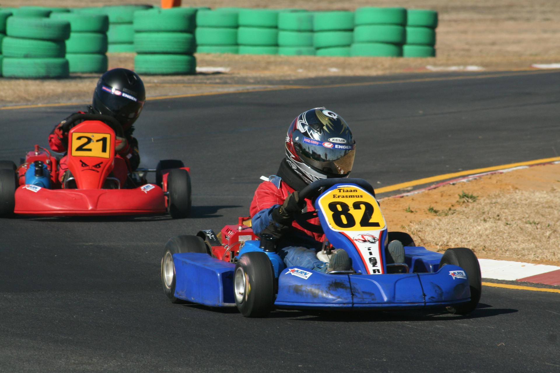 Competitive go-kart race with drivers maneuvering corners on a sunny day.