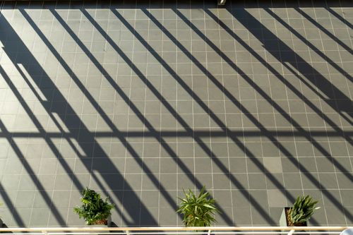 Free Sunlit shadows create patterns on a tiled balcony with potted plants, offering an artistic view. Stock Photo