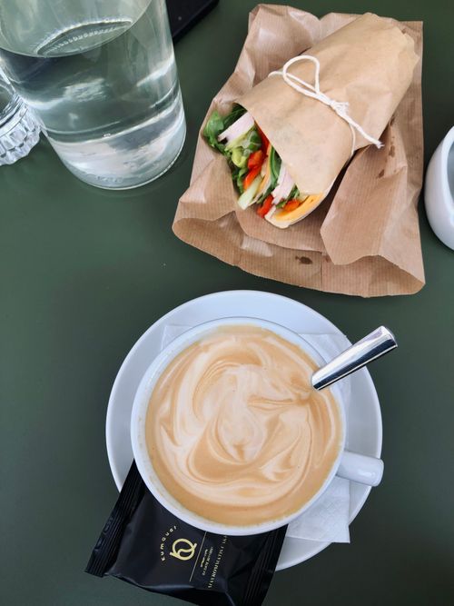 Free A savory latte paired with a fresh vegetable sandwich on a green table. Stock Photo