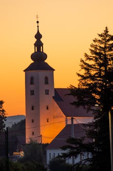 Stunning sunset silhouette of a historic church tower in Styria, Austria, showcasing tranquil autumn colors.