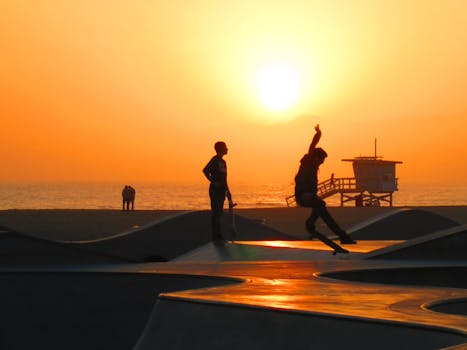 Skateboarders silhouetted against a vibrant sunset by the beach, capturing motion and tranquility.