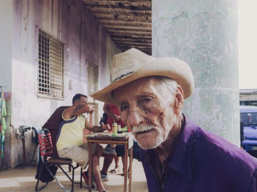Free Senior man wearing cowboy hat and purple shirt in outdoor setting with others. Stock Photo