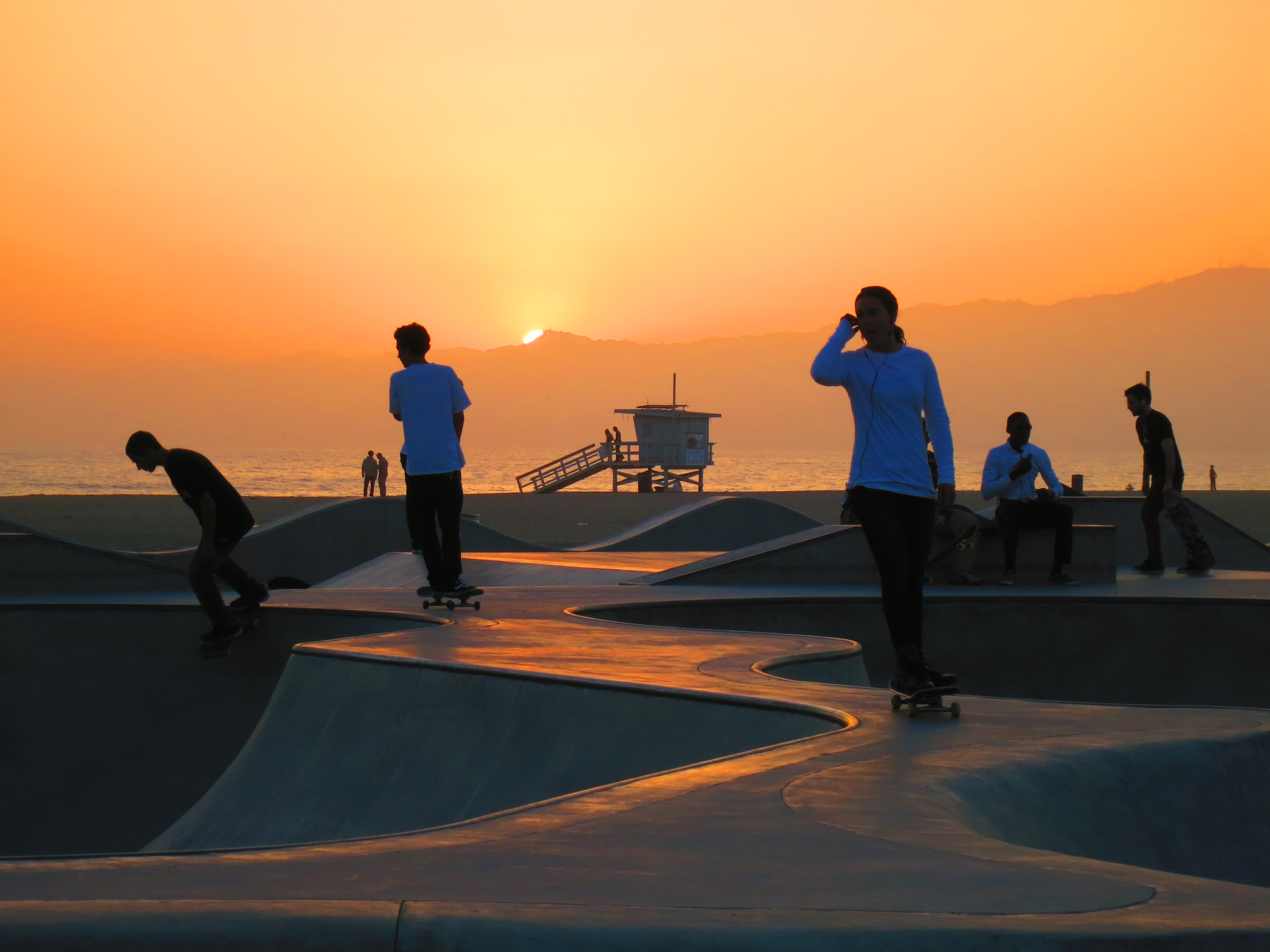Silhouetted skateboarders capture the California vibe at Venice Beach Skatepark against a stunning sunset backdrop.