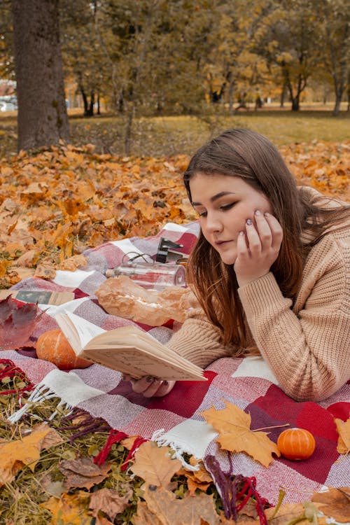 A Woman Reading a Book while Lying Down on a Picnic Blanket