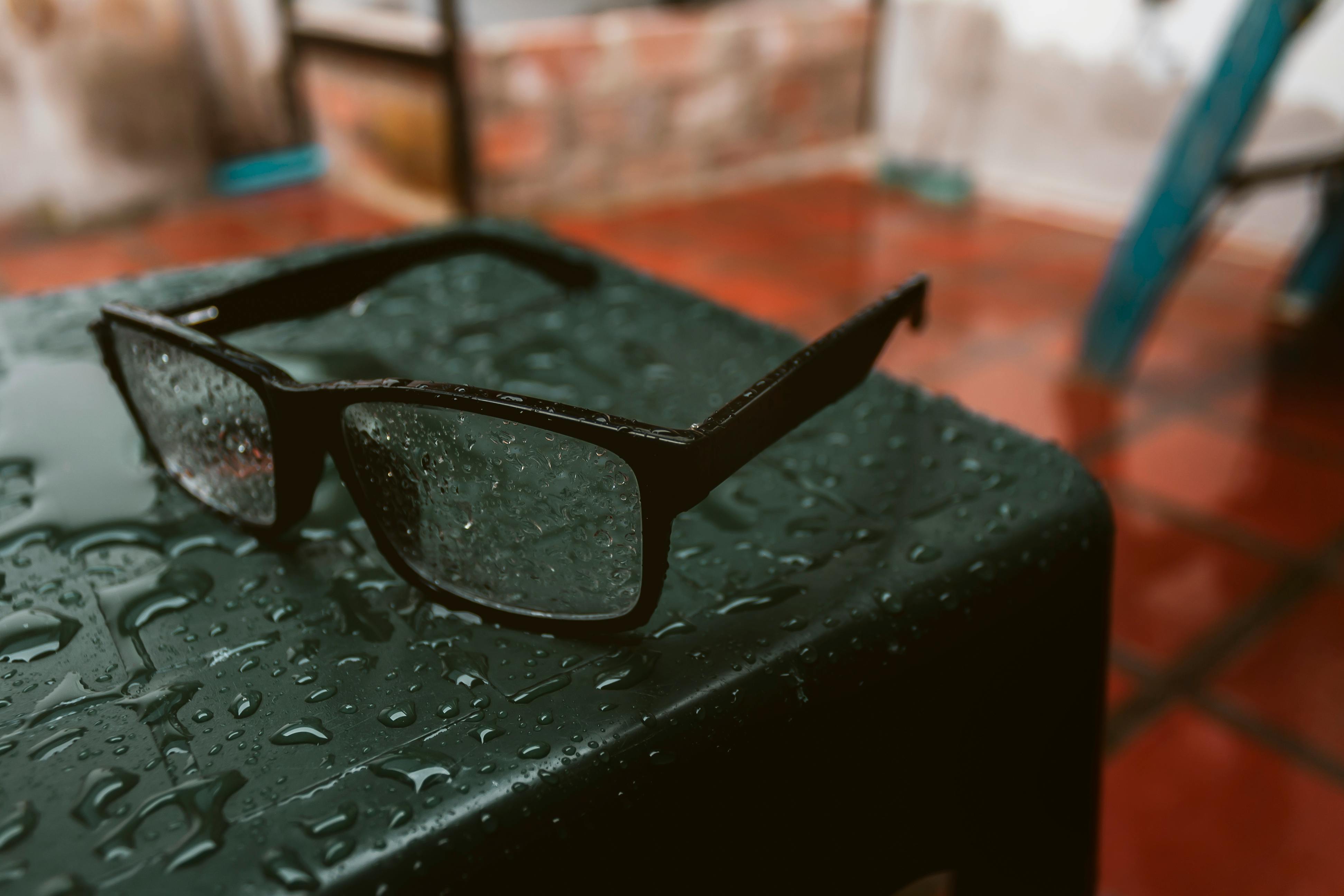 Close-up of eyeglasses covered with water droplets on a wet table indoors.