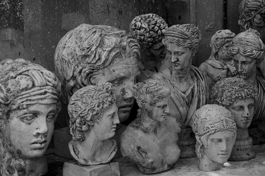 A group of vintage stone head bust sculptures in grayscale, depicting ancient figures.