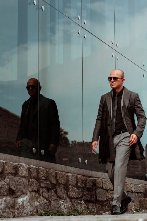 Free Confident businessman in sunglasses walking by a modern glass building in Turkey, exuding style and professionalism. Stock Photo