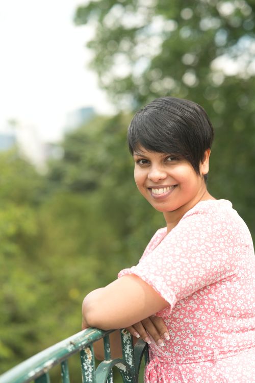 Free A woman in a floral pink dress smiles while leaning on a railing outdoors. Stock Photo