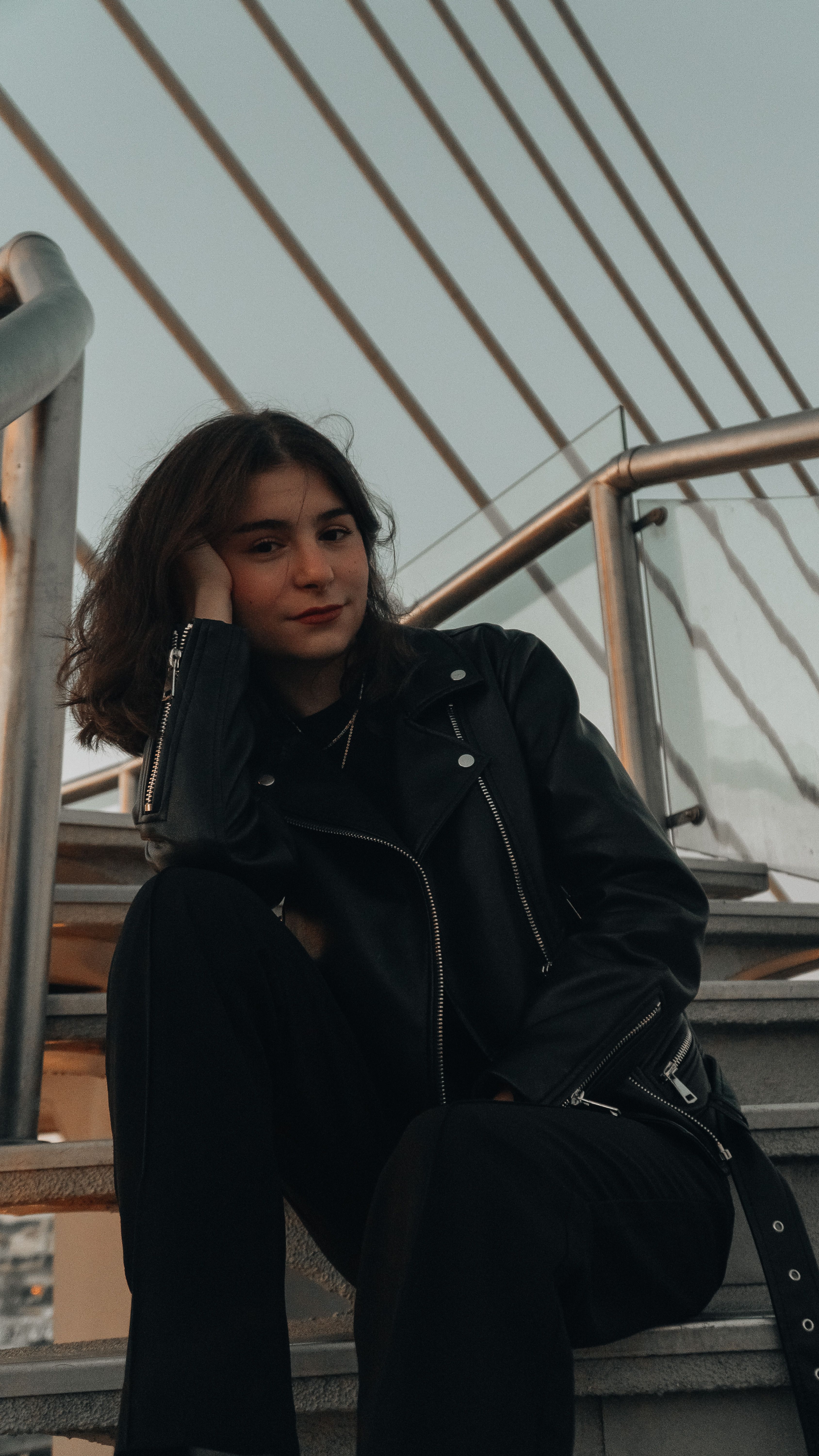 Stylish woman in a leather jacket sitting on a bridge in İstanbul, showing urban fashion.