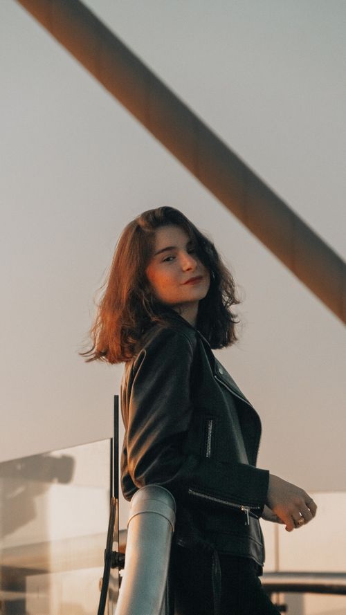 Free Young woman in black leather jacket standing on a balcony with glass and metal railings Stock Photo