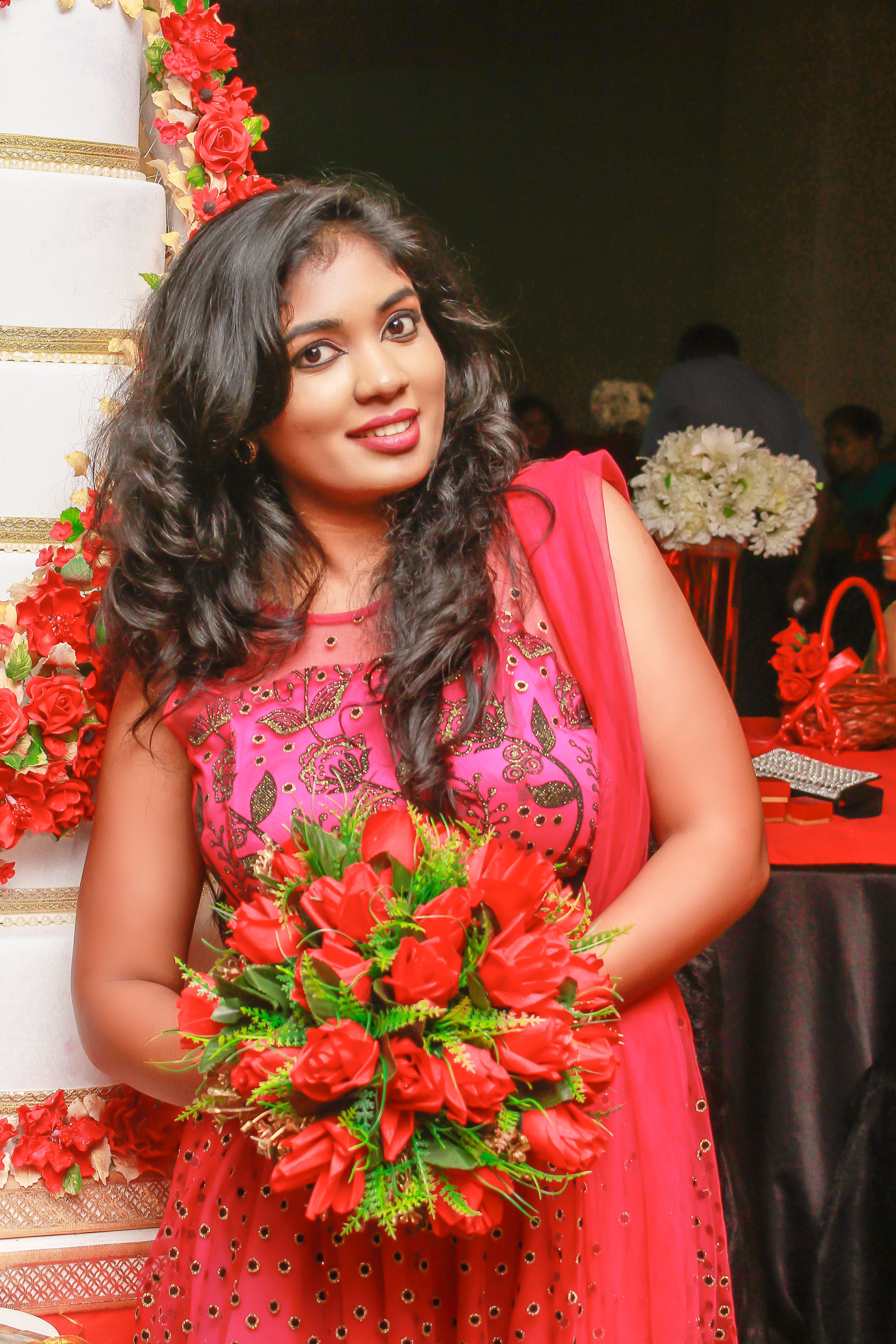 Elegant woman in red dress holding a flower bouquet at a festive event in Sri Lanka.