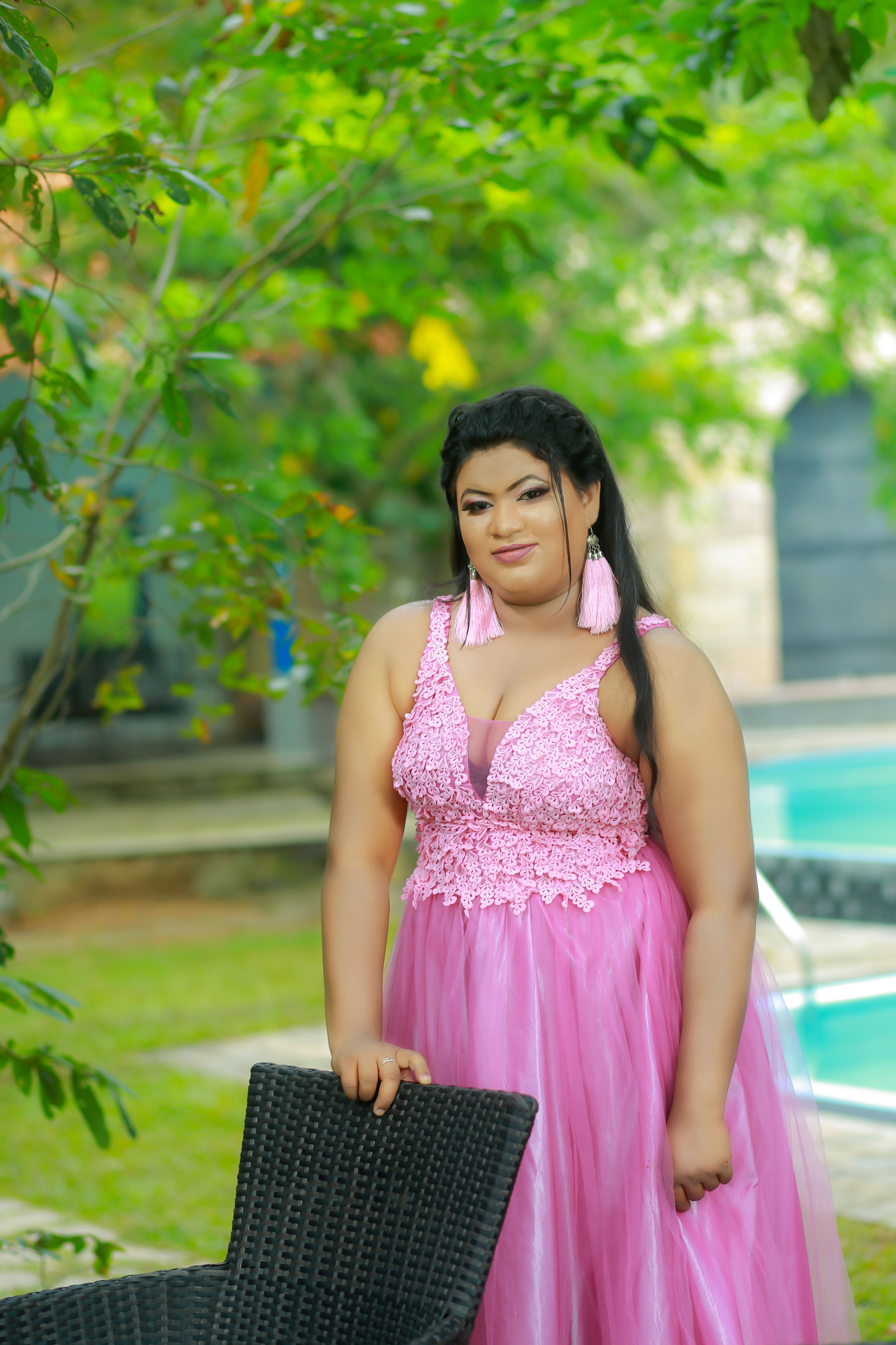 Stunning woman in a pink gown stands elegantly by a pool in Sri Lanka, surrounded by greenery.