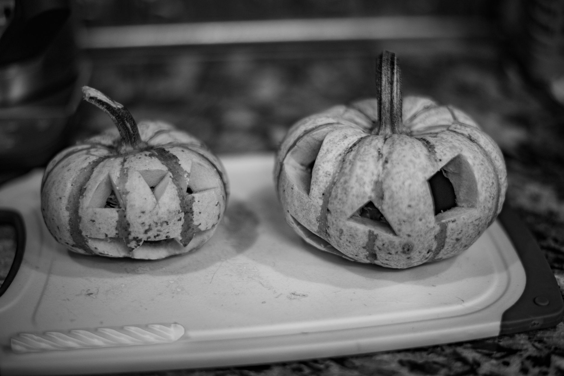 Monochrome image of carved pumpkins on a chopping board exuding a classic Halloween vibe. — free online jigsaw puzzle on JigsawPuzzlesFreeOnline.org