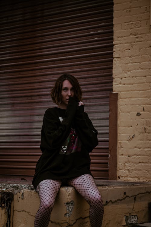 Woman in Black Sweater Sitting Near the Metal Shutter 