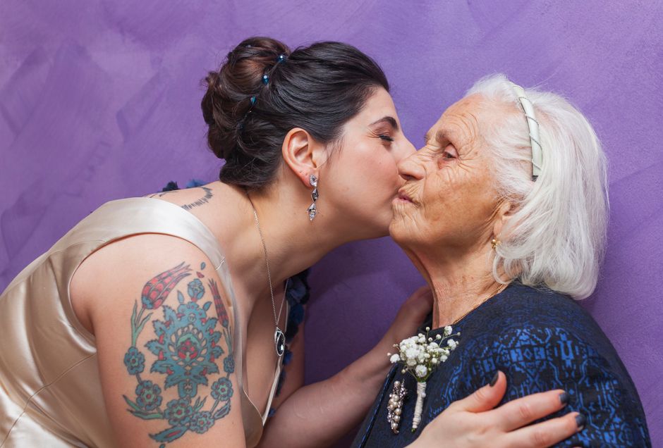 A young woman affectionately kisses her elderly grandmother on the cheek indoors.
