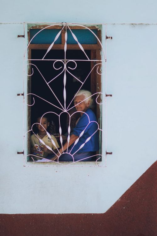 Free Elderly woman and young girl smiling behind a barred window of a house. Stock Photo