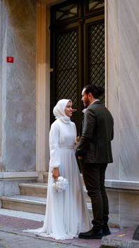 Beautiful wedding portrait of a Muslim bride and groom standing at a grand architectural entrance.