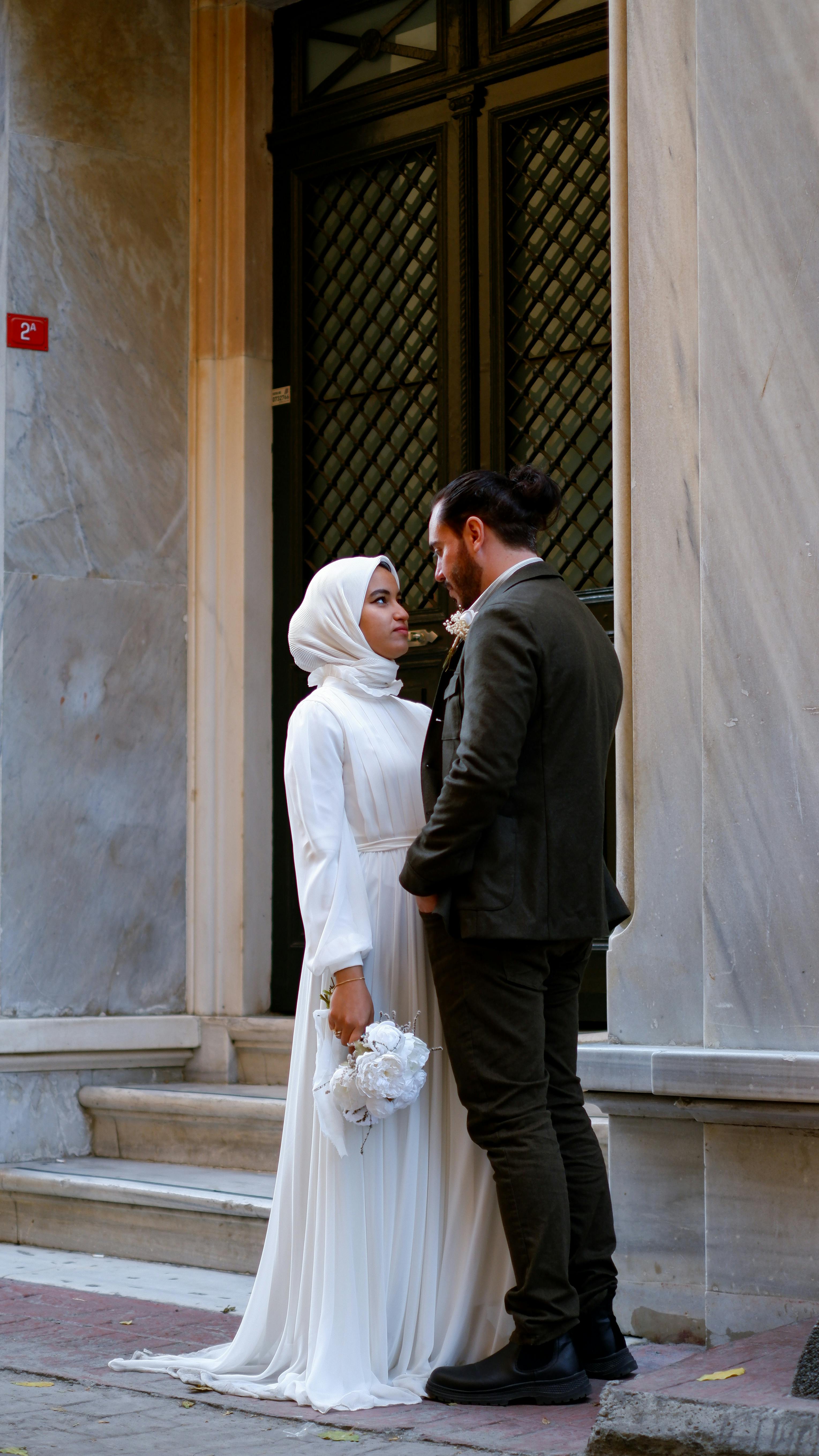 Newlywed couple standing in front of urban facade, sharing an intimate moment.