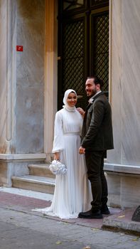 A sophisticated Muslim couple poses joyfully at their wedding in traditional attire, captured outdoors.