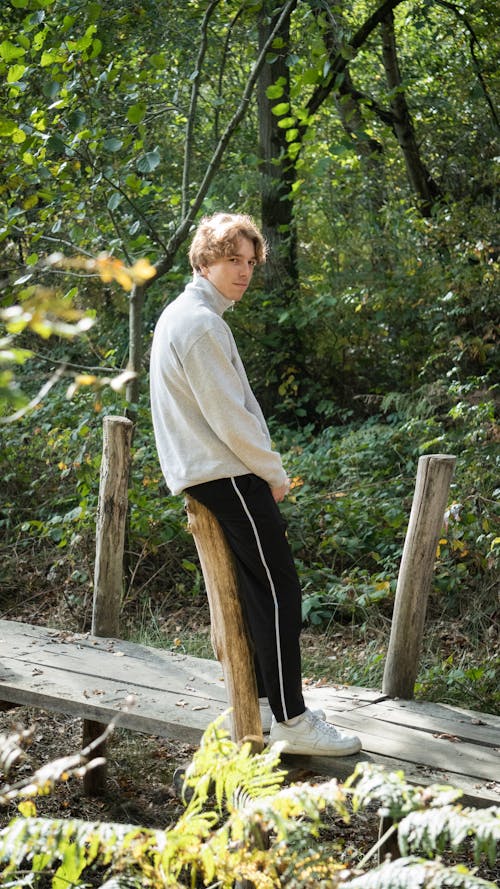 A Man in Turtleneck Sweater Standing on a Wooden Bridge at the Forest
