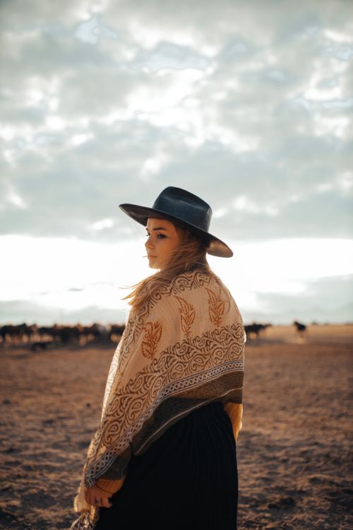 Free Woman in wide-brimmed hat and shawl on a serene landscape during sunset. Stock Photo