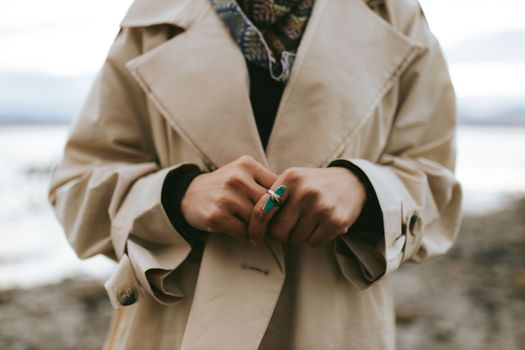 Woman wearing a trench coat and turquoise ring. Captured in a serene outdoor setting.
