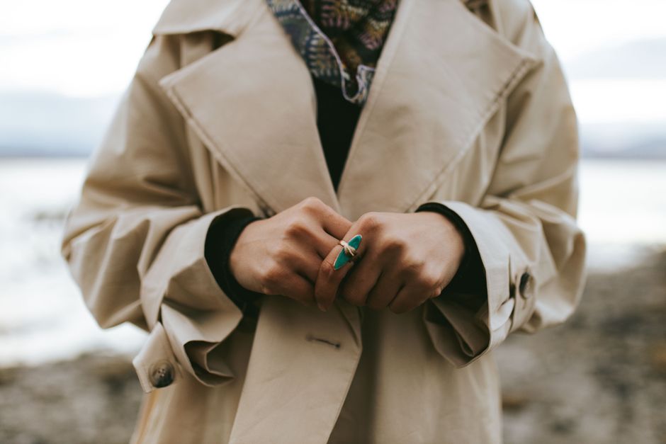 Woman wearing a trench coat and turquoise ring. Captured in a serene outdoor setting.