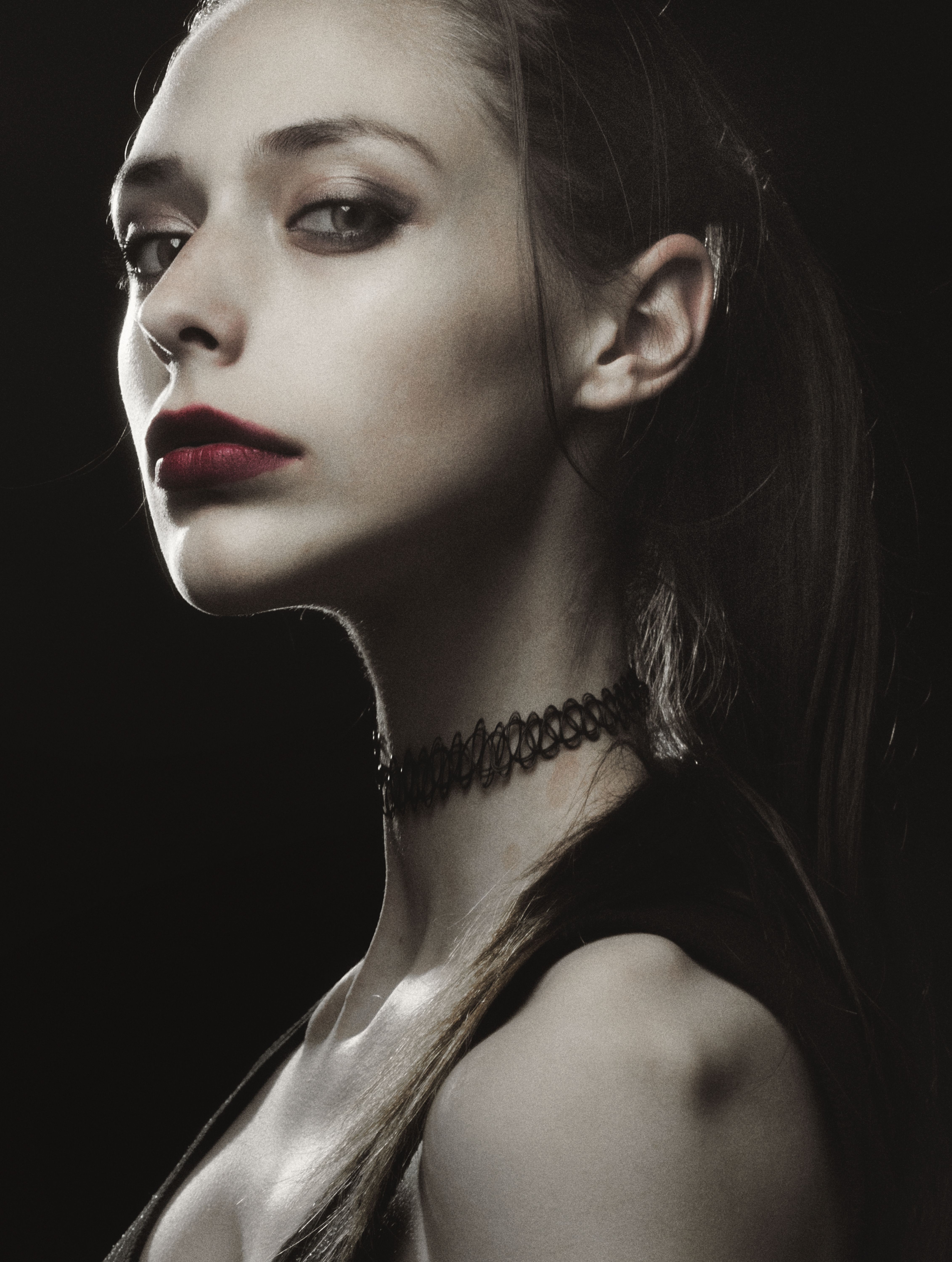 Dramatic portrait of a woman with red lipstick and choker, captured in a studio setting.