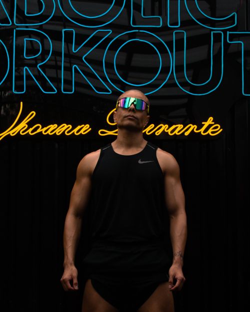 Free A muscular man poses confidently in front of a neon gym sign, embodying strength and fitness. Stock Photo