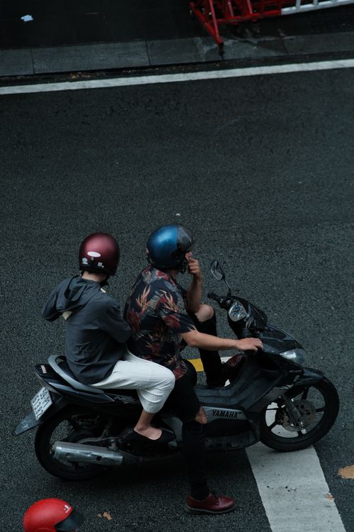 Free Two individuals with helmets riding a motorcycle on a city street, viewed from above. Stock Photo