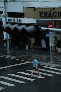 A person walks across a crosswalk on a rainy day in the city, beneath a traffic light.