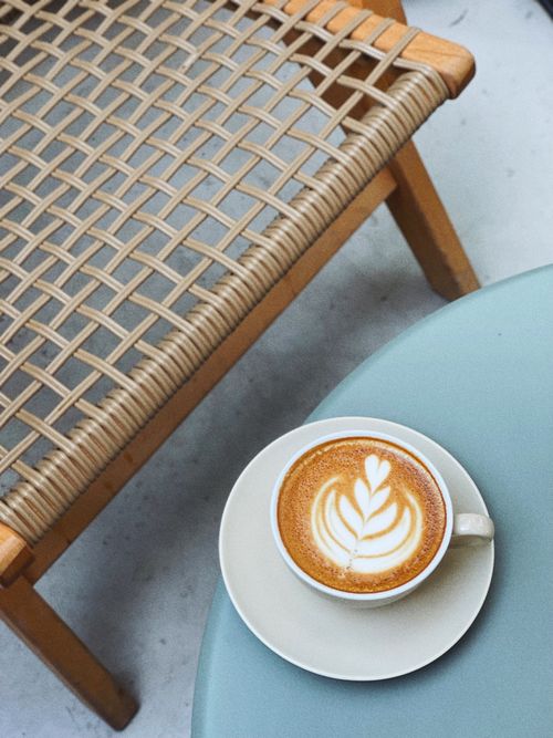 Free A delicate latte with art served on a stylish coffee table next to a woven chair. Stock Photo