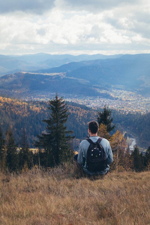 Man in Blue Shirt with Backpack Sitting on Brown Grass