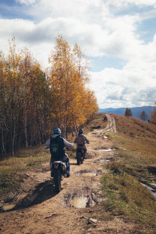 Free Two people riding motorcycles on a dirt road through autumn forest scenery. Stock Photo