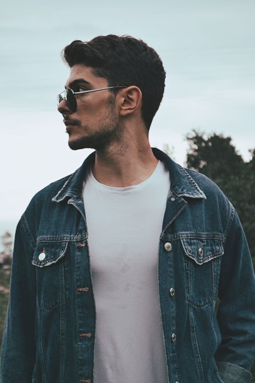 Free Stylish man wearing sunglasses and a denim jacket in an outdoor setting. Stock Photo