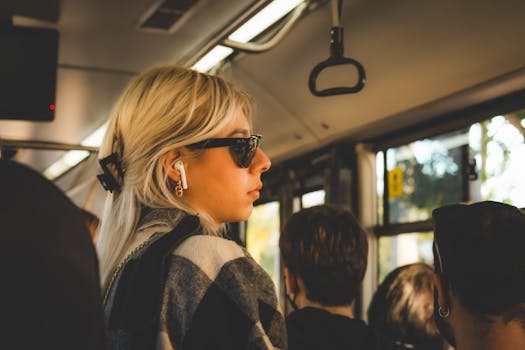 Young woman with blonde hair and sunglasses commuting on a bus, listening to music.