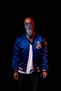 Portrait of a bald man in a blue jacket and bandana on a black background.