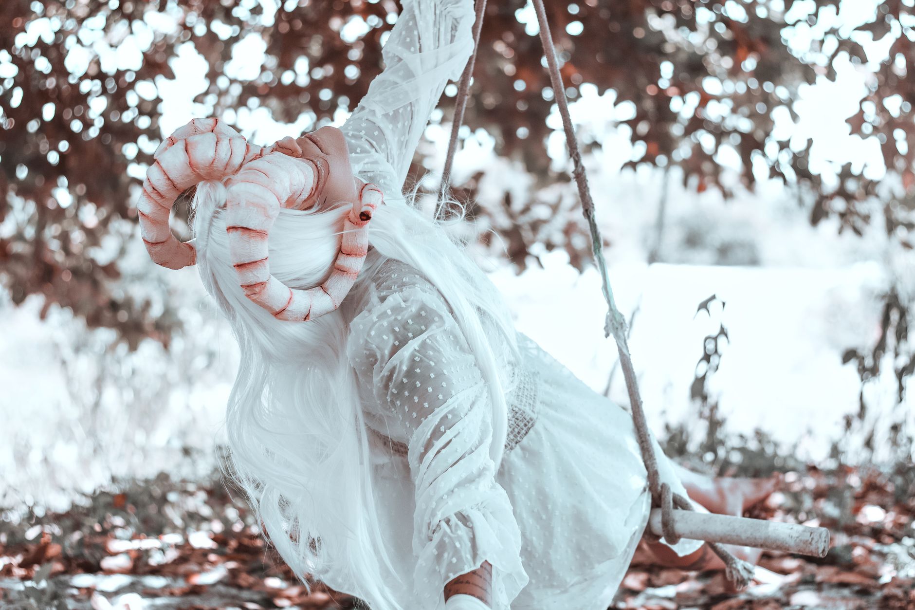 A woman in a fantasy costume with horns swings outdoors in a mystical scene.