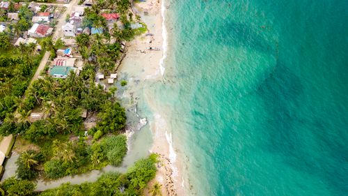 Free Drone shot of turquoise waters meeting a tropical beach lined with palm trees and a coastal village. Stock Photo