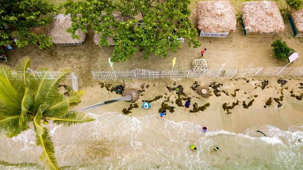 Aerial shot of tropical beach with nipa huts, palm trees, and seawaves.