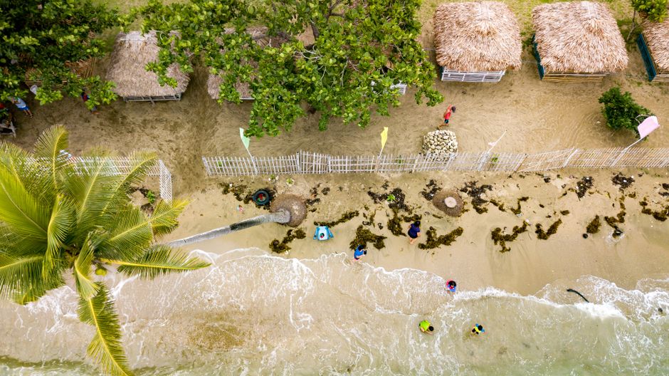 Aerial shot of tropical beach with nipa huts, palm trees, and seawaves.