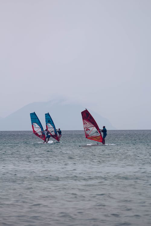 Unrecognizable people balancing on windsurf boards on calm sea water against cloudy gray sky