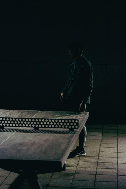 Free Silhouetted man playing table tennis outdoors at night, creating a moody vibe. Stock Photo