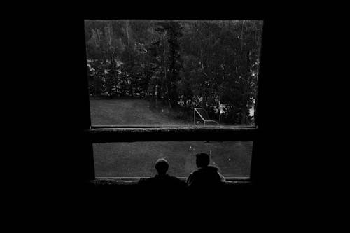 Grayscale Photo of Two People Looking Out the Window
