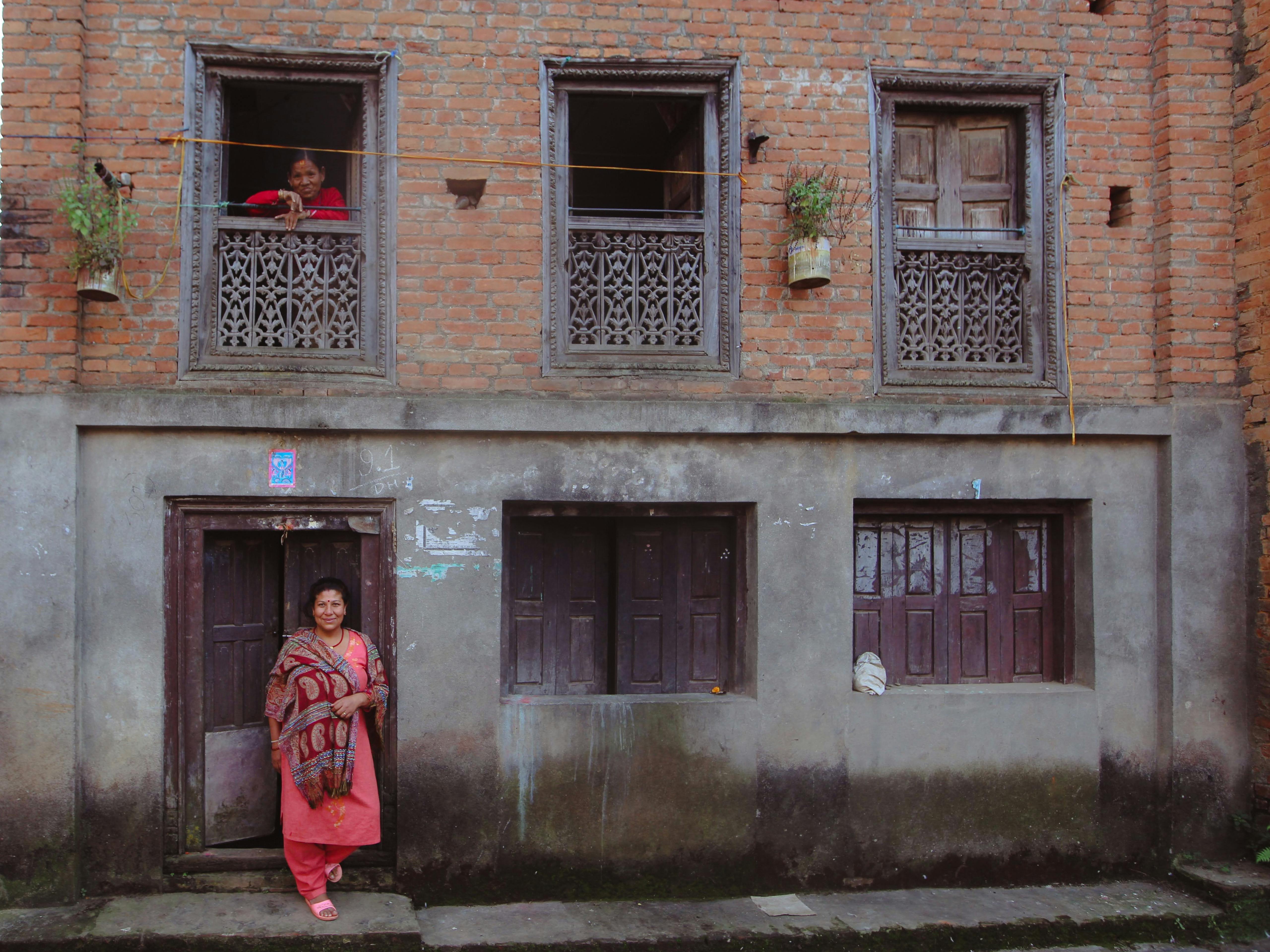 A traditional brick home facade in Nepal with two women, highlighting cultural architecture and daily life.