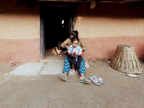 Free A woman styles her daughter's hair outside a traditional rural house, showcasing everyday family life. Stock Photo