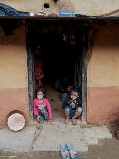 Free Two children sitting in a rustic doorway with a woman partially visible inside. Stock Photo