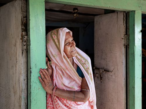 Free A senior woman in a traditional sari smiles while leaning in a doorway. Stock Photo